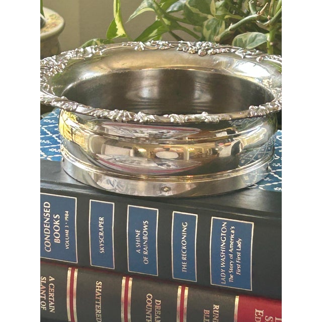 Handsome vintage silver-plated wine bottle coaster featuring an ornate repoussé floral and scroll border surrounding a...