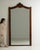 This mirror carries genuine presence, its dark walnut frame with carved crest, arched tall immediately setting the tone...