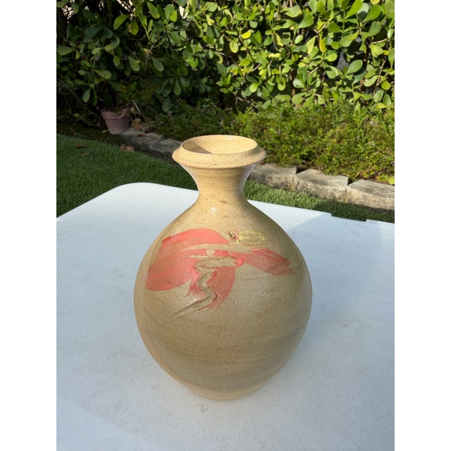 A handcrafted studio pottery bottle vase featuring a warm buff stoneware body accented with expressive coral and ochre...