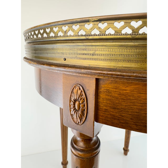 A beautiful vintage Louis XVI-style side table featuring a warm mahogany frame, inset cream marble top, and beautifully...