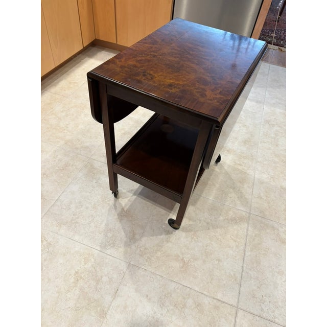 This wheeled tea trolley or pembroke table is believed to be made of mahogany with a walnut burl veneer top, a lower...