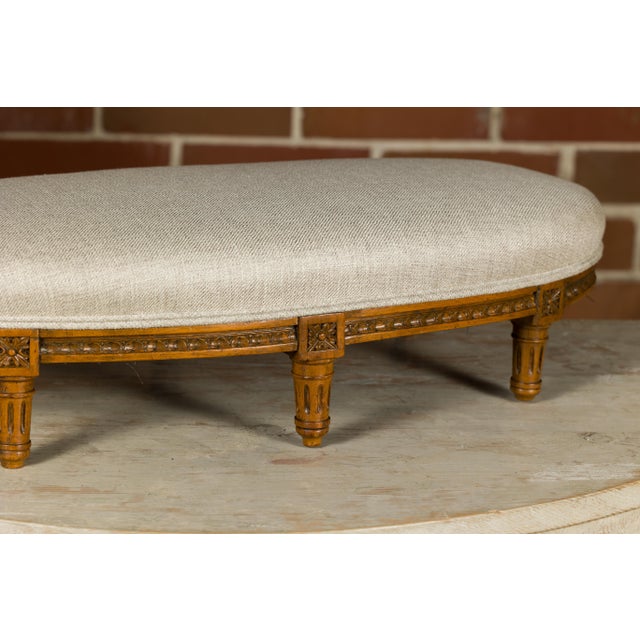 A French Louis XVI style walnut footstool from the 19th century with custom linen upholstery. This exquisite Louis XVI-...