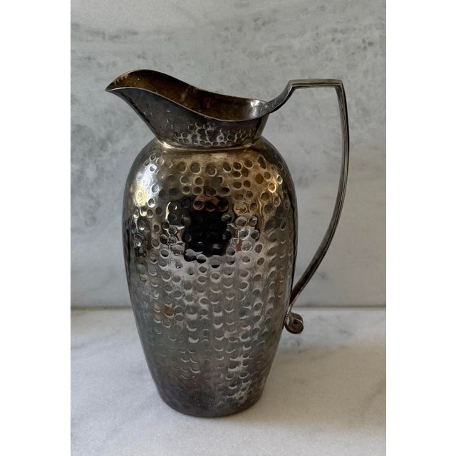 Vintage hammered silver-tone metal water pitcher with a curved handle and flared spout. Heavy in weight. Would be...