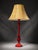 Decorative table lamp featuring a glossy deep red base with an elegant vintage-style shape and a warm beige textured...