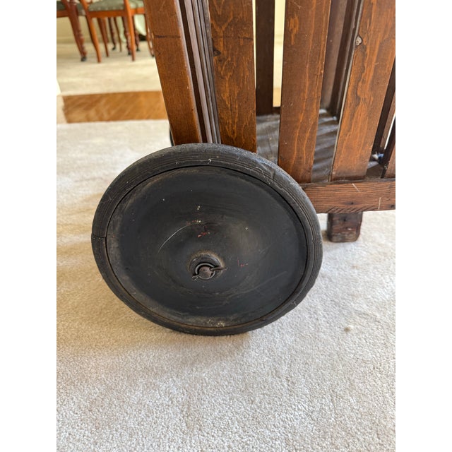 This is a wooden slat-construction rolling pull basket featuring a vertical handle, open slatted sides with crenellated...