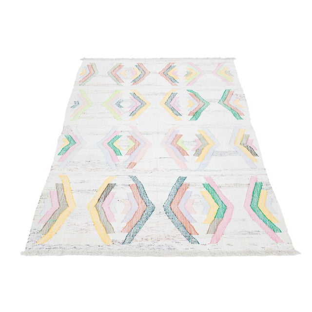 This rug features a modern Kilim flatweave design made from wool. It has a beige base with a geometric pattern in various...