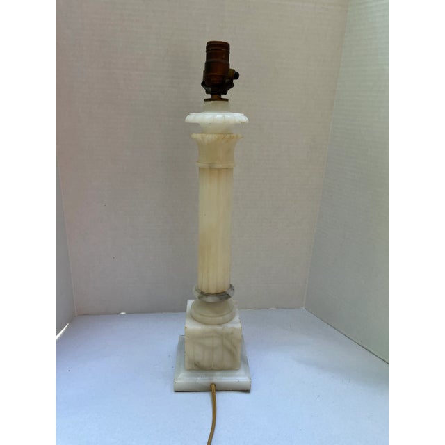 A single white carved alabaster marble neoclassical column with square base and stylized Corinthian capital mounted as a...