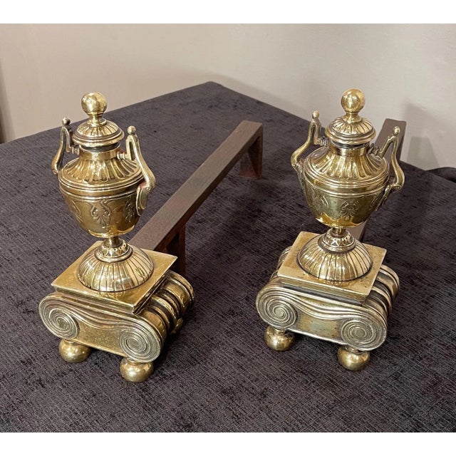 A Pair of Brass Andirons, of diminutive proportions Urn form, raised on scrolled base with Brass ball feet Tightened...