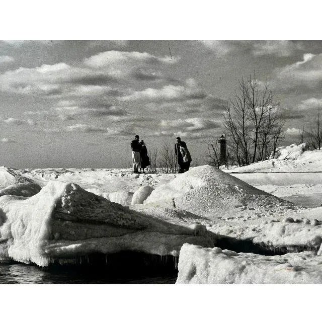 A gorgeous 1950s black/white photo of Lake Michigan in the winter. Four visitors, clearly cold and underdressed, take in...
