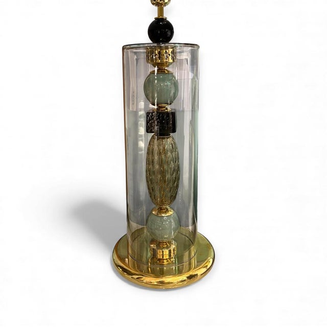 Italian Murano glass table lamp with a gold-tone brass base. It features decorative interior elements and a textured...