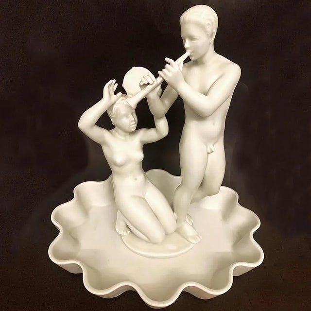 Beautifully finished in an ivory-hued glaze, this ambitious and rare sculptural grouping of a Pan and Nymph with flute and...