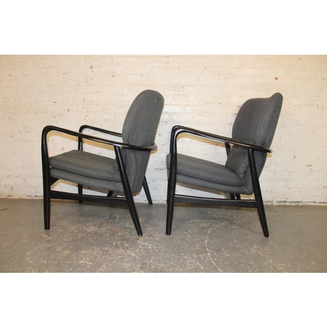 Pair of mid-century modern styled armchairs. Grey fabric body set in a black wood frame. Sculpted frame goes around the...