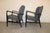 Pair of mid-century modern styled armchairs. Grey fabric body set in a black wood frame. Sculpted frame goes around the...