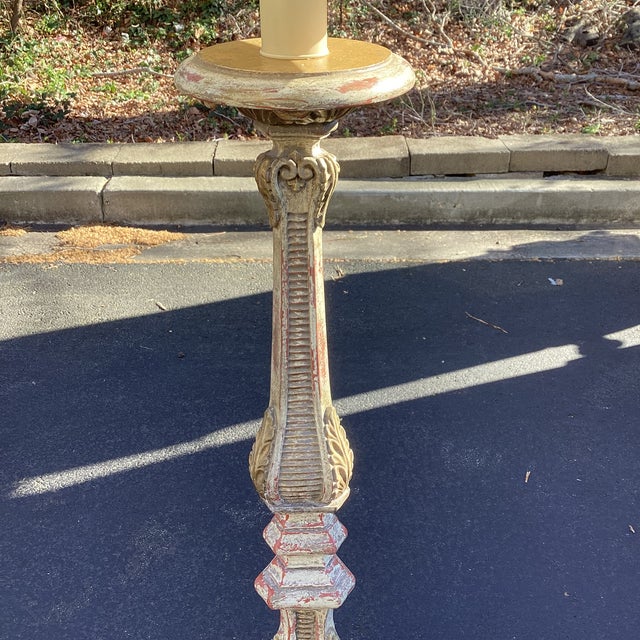 A striking Italian-style carved wood floor lamp featuring an elegantly turned and fluted column rising from a sculptural...