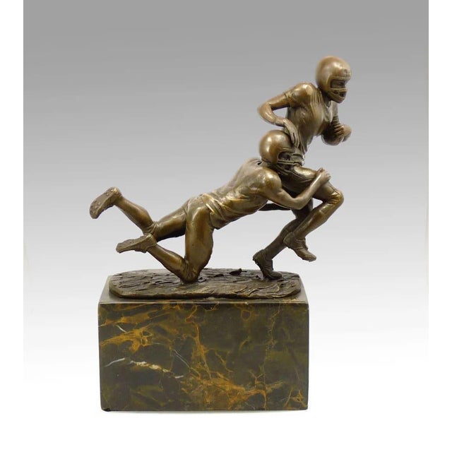 This bronze statue of a football player, captures a moment of poised action, with the ball held under the player’s arm....