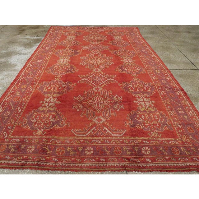 A Vintage Turkish Oushak room size carpet with a central column of lozenges, cruciforms, and bent leaf brackets, flanked...
