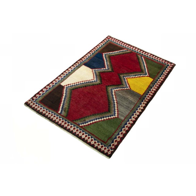 A unique hand-knotted Gabbeh nomad rug with bold colors and geometric pattern. The combination of deep red, blue, green...