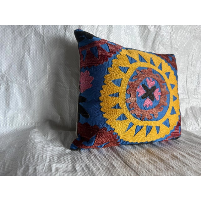 A vibrant vintage Suzani pillow featuring a striking circular medallion pattern hand-embroidered in golden mustard,...