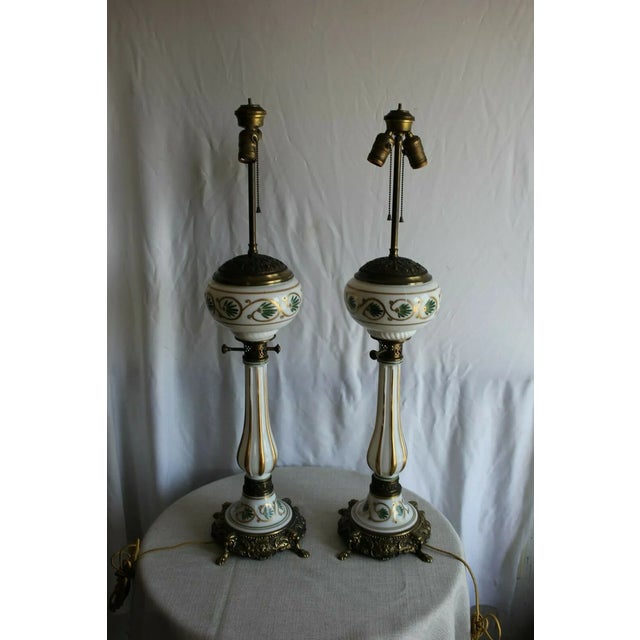 Elegant pair of Regency style porcelain lamps each one beautifully painted and gilded, resting on ornate brass bases. They...