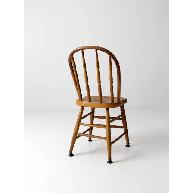 Circa 1920 spindle back chair featuring beautifully turned spindles and legs paired with black metal glides. The warm...