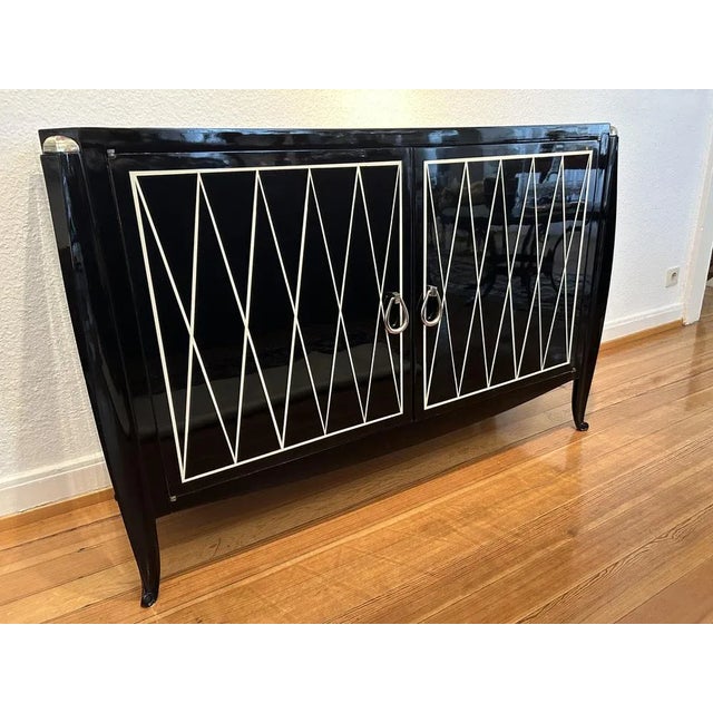 The sideboard, formally in the elegant style of Émile-Jacques Ruhlmann's furniture, is painted high-gloss black with a...