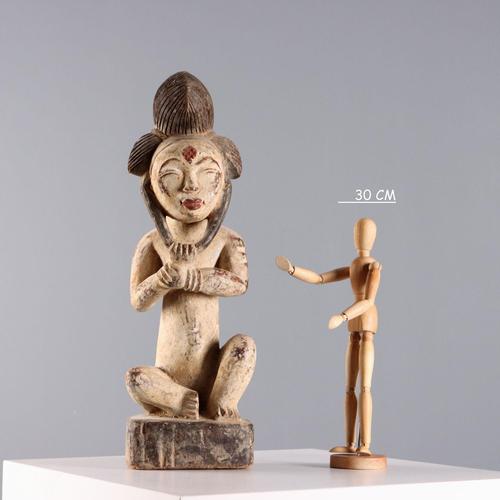 Wooden figure of a seated ancestor with a white kaolin patina, a tripartite hairdo, and frontal scarification identifying...