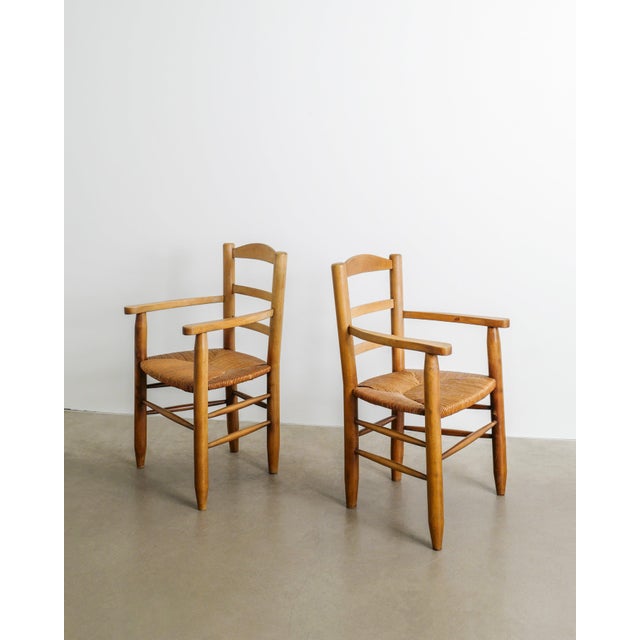 A rare and rustic pair of french mid century wooden armchairs in stained elm with decorative matching straw seats produced...