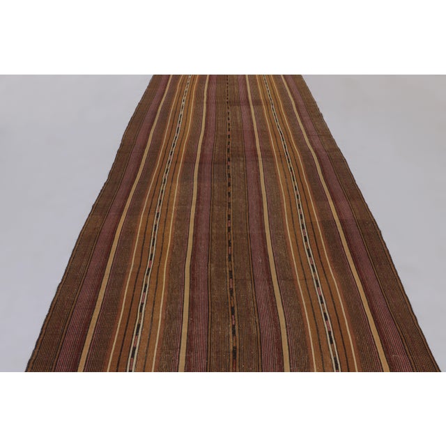 Made with handwoven wool circa 1950-1960, this 6x12 vintage flat-weave gallery runner Kilim is a particularly atmospheric...