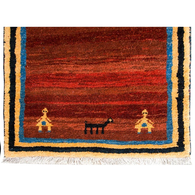 A bold vintage Persian Gabbeh rug with a abrash cranberry field with a central stylized indigo goat, more goats and people...