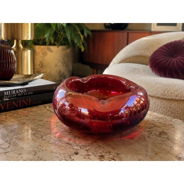 A striking large-scale handblown art glass ashtray or catchall bowl in a rich ruby red hue, featuring an elegant...