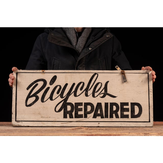Double-sided painted wood advertising sign reading "Bicycles Repaired" in bold black lettering against a cream ground. The...