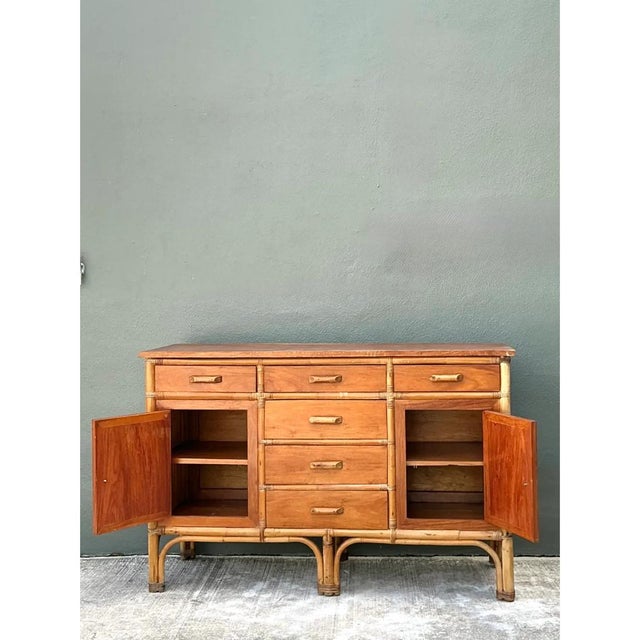 This vintage credenza is a low, rectilinear case piece wrapped in a framework of honey-toned rattan and bamboo, with the...