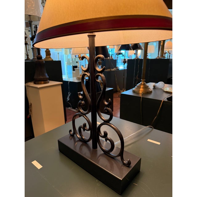 A Haig table lamp featuring an ornate openwork metal base with symmetrical scrollwork and a dark brass bronze finish....