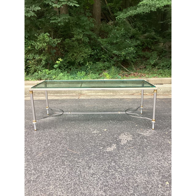The rectangular glass top rests within a gilt-brass frame, supported by steel legs with brass accents and joined by a open...