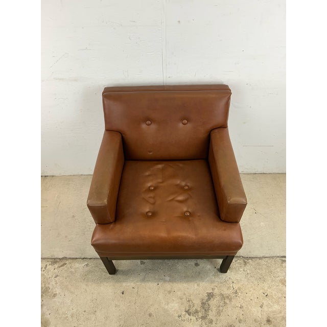 This mid century modern lounge chair features brown vinyl upholstery with tufted seat and back atop a solid walnut base.
