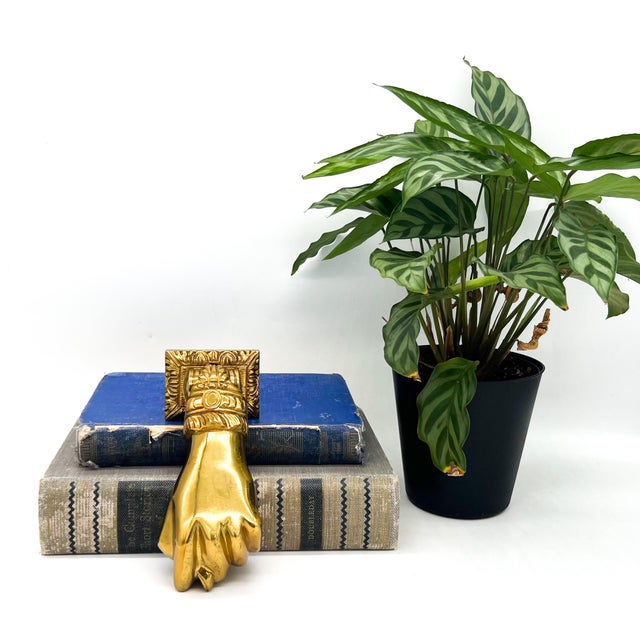 Eye-catching, vintage brass hand door knocker featuring a sculptural clenched hand with detailed cuff and decorative...