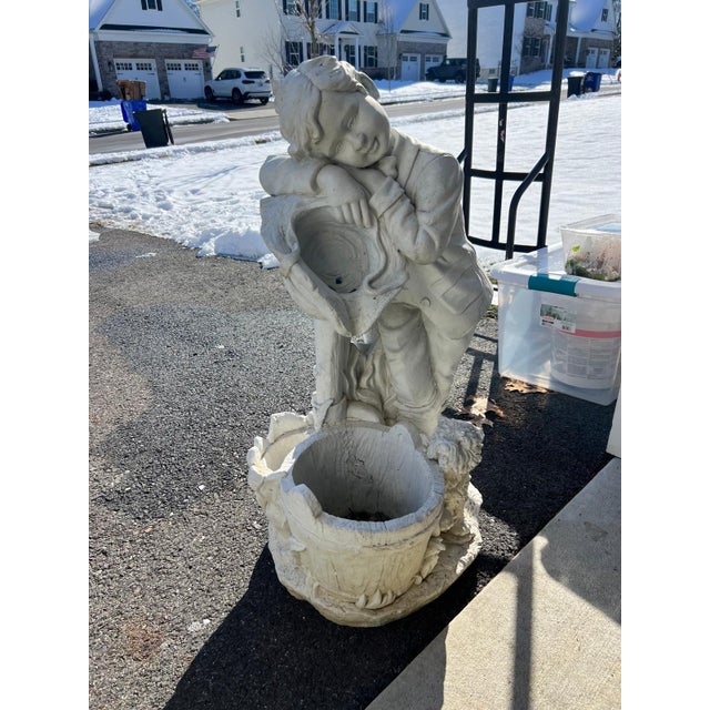 This charming vintage garden sculpture depicts a young boy resting against a large pitcher, a timeless motif drawn from...