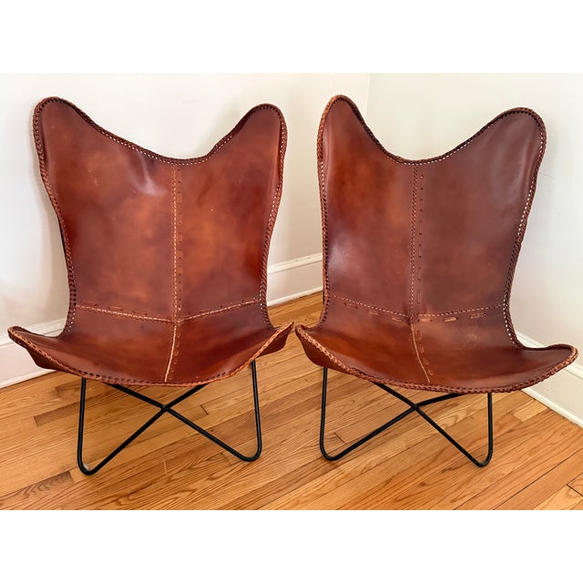 This pair of vintage butterfly chairs with worn leather seats are the perfect mix of modern and rustic. Warm mahogany-...