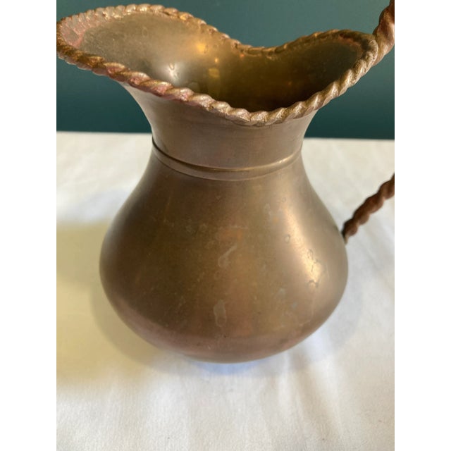 This vintage hammered brass pitcher features a beautifully sculpted form, a wide scalloped lip, and an ornate twisted...