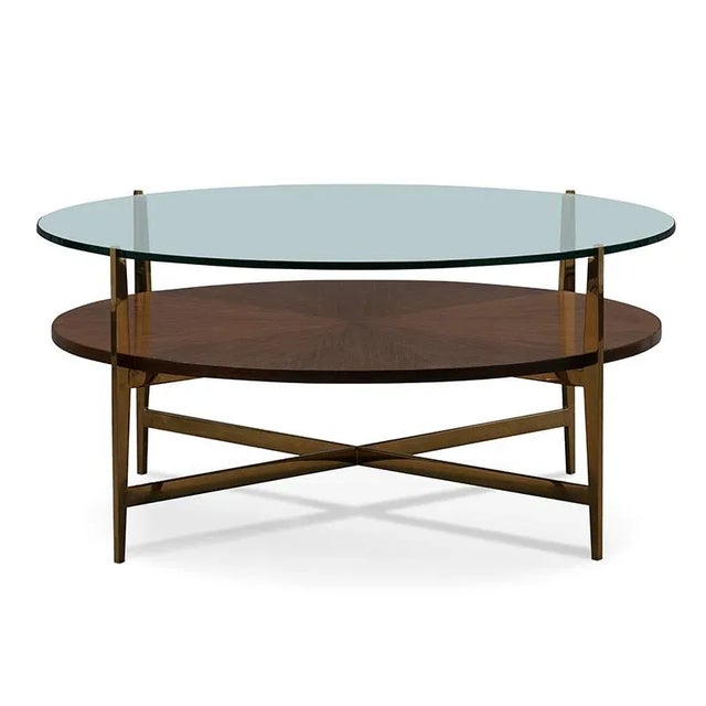 A round glass top is elevated on brass legs joined by a middle walnut shelf. The brass legs are joined by a low stretcher.