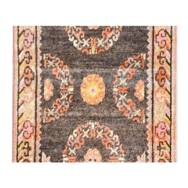A petite and sweet early 20th century Central Asian Khotan rug with two floral medallions woven in coral, white, gold, and...