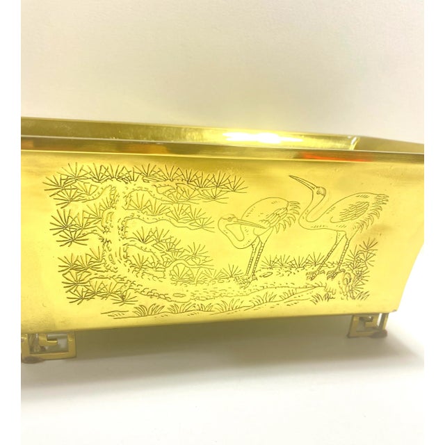 A beautifully engraved Asian brass planter featuring traditional landscape motifs and a distinctive footed base. The...