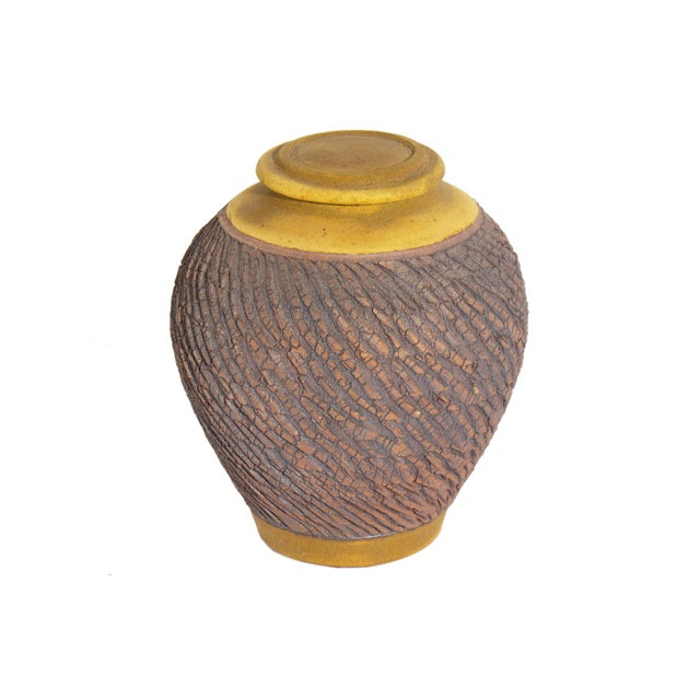 A studio pottery jar by the American ceramicist Barry Vantiger. This rounded jar features a textured, brown design, which...