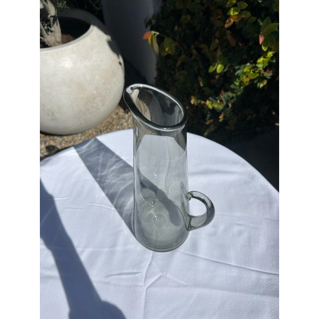 Vintage smoky gray glass pitcher featuring a tall, elegant silhouette with a softly flared spout and applied curved...