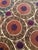 Hand-embroidered Suzani panel from Uzbekistan — rows of terracotta and plum round medallions on a deep brown ground with a...