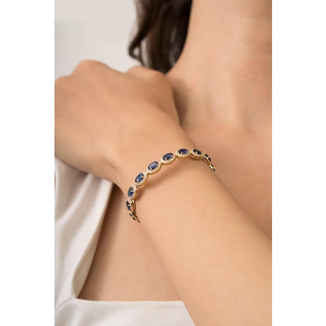 This tennis bracelet features 10.02 carats of oval blue sapphire set in 18K yellow gold. Each measuring approximately 6 x...