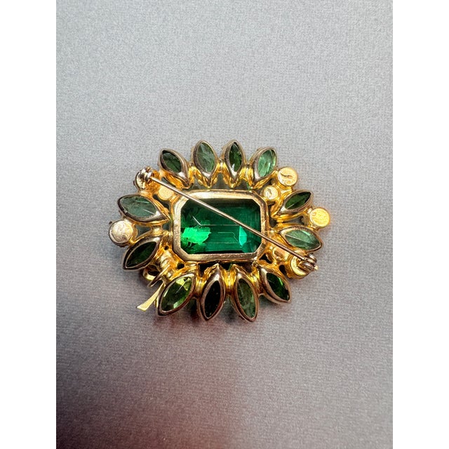 A vivid 1960s DeLizza & Elster brooch designed in a rich emerald‑green palette. The rectangular faceted center stone is...