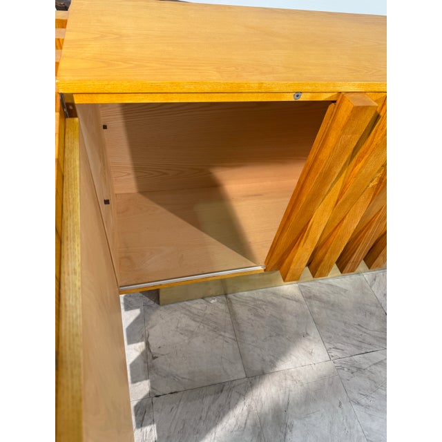 This contemporary credenza features a bold geometric facade crafted from solid wood slats arranged in an angled, rhythmic...