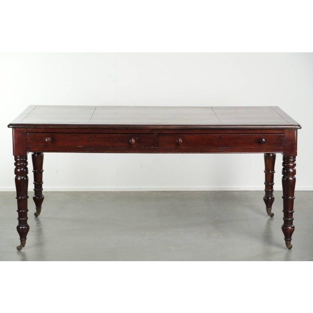 This antique English writing desk features a warm wood tone and a dark brown leather top with gold accents. The desk has...