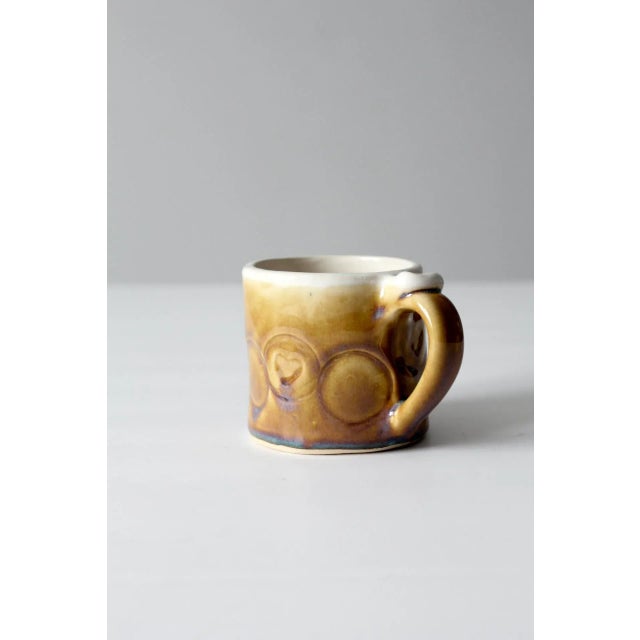 This hand-crafted studio pottery mug from Daybreak Pottery features a warm golden brown and cream glaze with stamped...